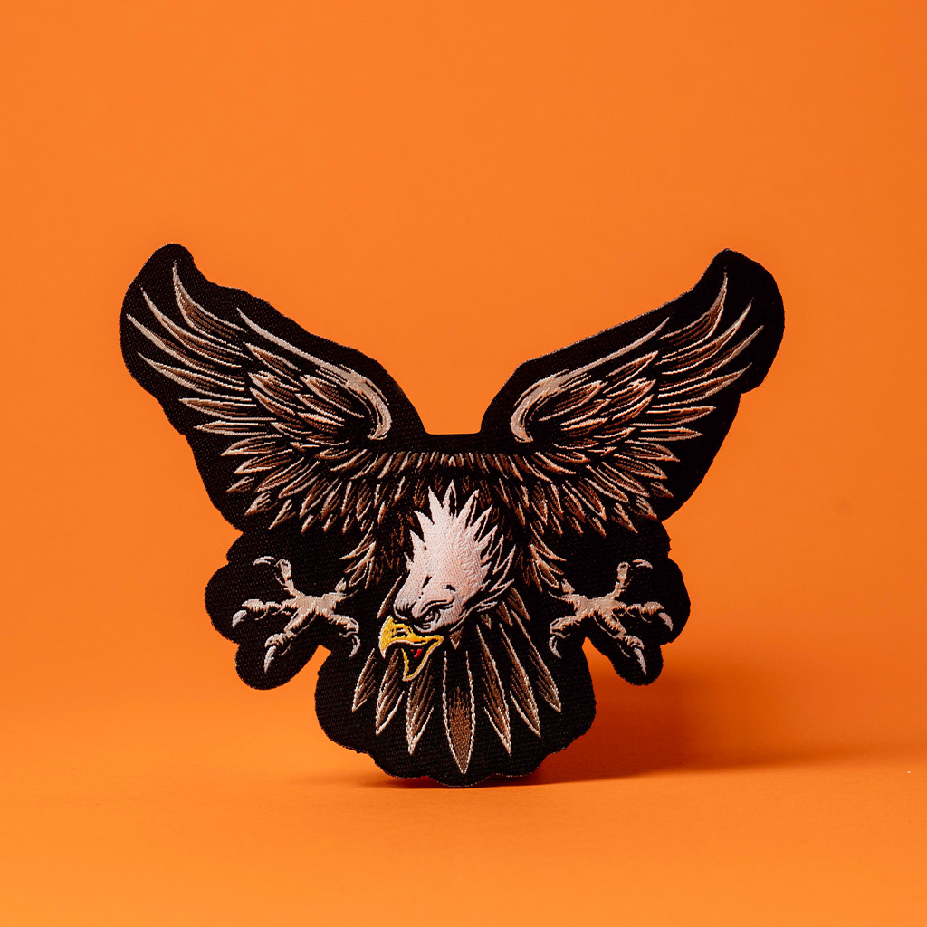 Schwarz-brauner Adler Stickaufnäher vor kräftigem Orange.