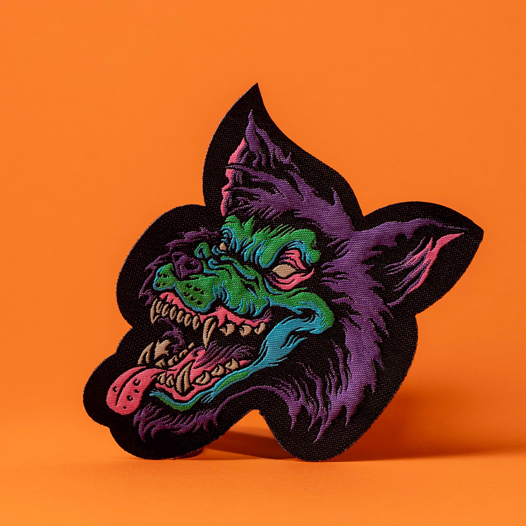 Lila-grüner Wolfsaufnäher auf einfarbigem orangefarbenem Grund.